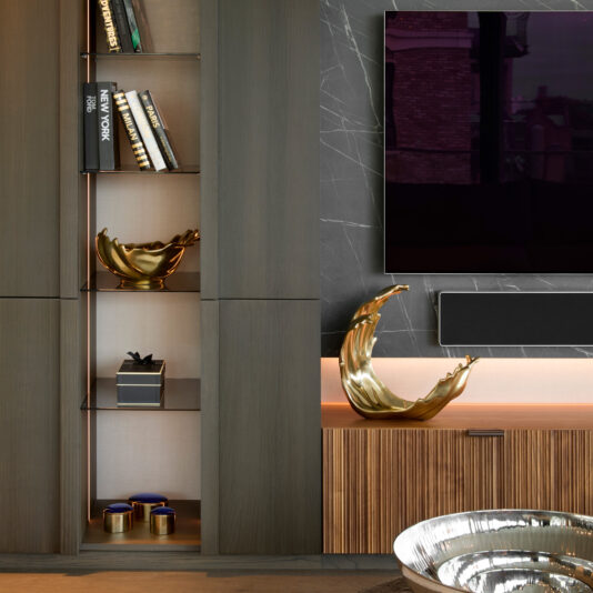 Luxury Decorative Wave Bowl A modern living room features dark wood shelves, books, gold bowls, small blue jars, a large wall-mounted TV, and a black marble wall with white veining accented by the Luxury Decorative Wave Ornament.