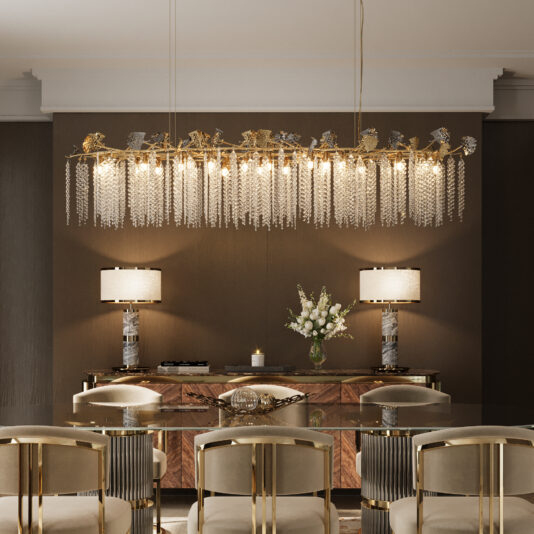Contemporary Leaf Chandelier With Crystal Drops An elegant dining room features a glass table, gold-accented chairs, and the Contemporary Leaf Chandelier With Crystal Drops. Matching lamps on a wooden sideboard and a vase of white flowers complete the neutral, sophisticated décor.