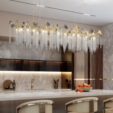Contemporary Leaf Chandelier With Crystal Drops A modern kitchen with marble walls and countertops features the Contemporary Wavy Tiered Chandelier (Copy) with gold accents and crystal strands above a sleek island topped with fruit and surrounded by neutral-toned chairs.