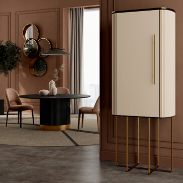 A modern dining room with the Round Contemporary Marble Effect Dining Table, pink chairs, and circular mirrors on a brown wall. A tall cream cabinet with gold legs stands to the right, while large windows with curtains brighten the space.