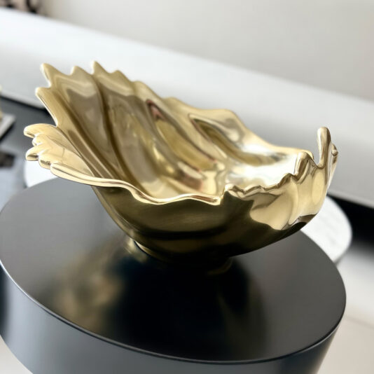 Luxury Decorative Wave Bowl A shiny gold Decorative Wave Ornament (Copy) with wavy edges sits on a round black tabletop in a modern, minimalistic setting.