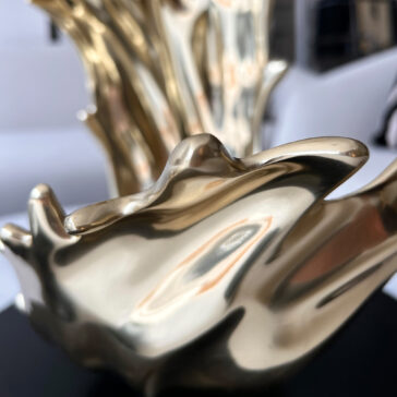 A close-up of a shiny, abstract golden sculpture with smooth, wavy surfaces reflecting light, evoking the elegance of the Set Of 3 Luxury Marble Candle Holders (Copy), with a blurred background emphasizing its intricate details.