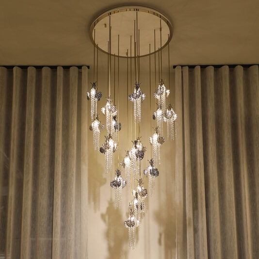 The Large Leaf Chandelier With Crystal Drops (Copy) features clusters of hanging glass and metallic lights from a round ceiling mount, set against soft, pleated curtains.