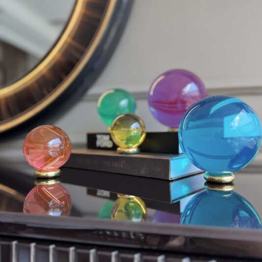 The Luxury Colourful Acrylic Ball Set includes vibrant blue, pink, yellow, green, and purple orbs on gold stands displayed on stacked books with a large round mirror in the background.