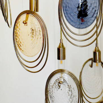 Modern Ceiling Light Inspired By The Sea The Modern Ceiling Light Inspired By The Sea features hanging pendants with circular, rippled glass shades in gold, clear, and blue, encircled by thin golden rings against a light background.