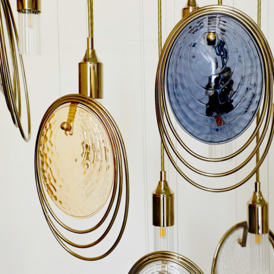Modern Ceiling Light Inspired By The Sea The Modern Ceiling Light Inspired By The Sea features hanging pendant lights with circular, textured amber and blue glass discs, accented by concentric gold rings, creating a striking modern design against a light backdrop.