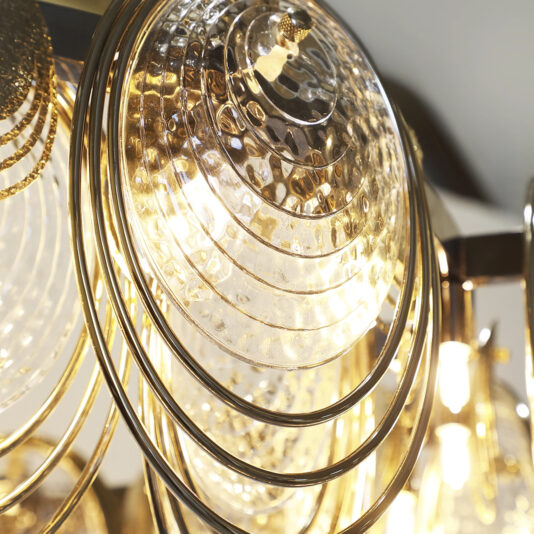 Modern Round Chandelier Inspired By The Sea Close-up of the Large Leaf Chandelier With Crystal Drops (Copy), showcasing circular, textured glass plates and gold metal rings that reflect warm light for a shimmering, elegant effect.