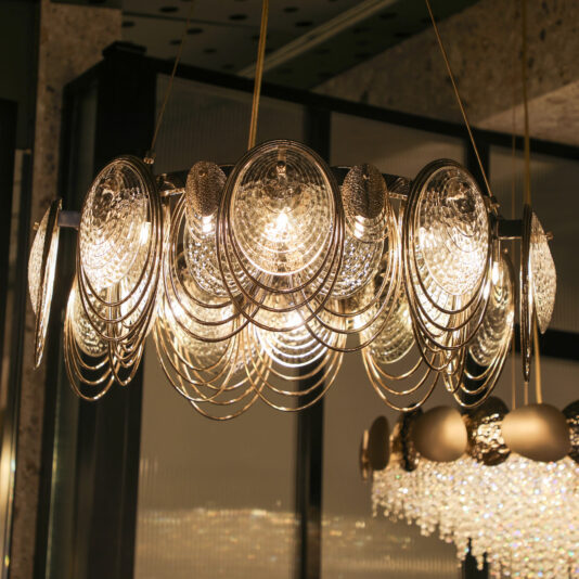 Modern Round Chandelier Inspired By The Sea The Large Leaf Chandelier With Crystal Drops (Copy) showcases circular glass and metallic accents with sparkling crystal drops, glowing warmly as it hangs from the ceiling in a contemporary interior.