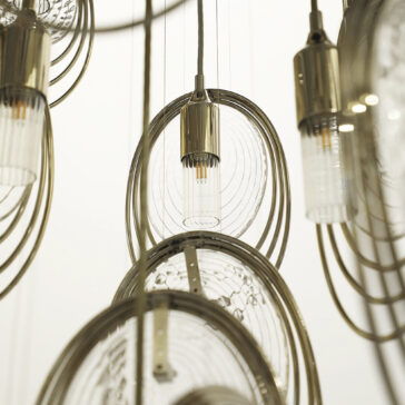 Modern Stairwell Chandelier Inspired By The Sea Close-up of the Modern Round Chandelier Inspired By The Sea (Copy), showcasing cylindrical bulbs, concentric metallic rings, and clear circular elements against a neutral backdrop.