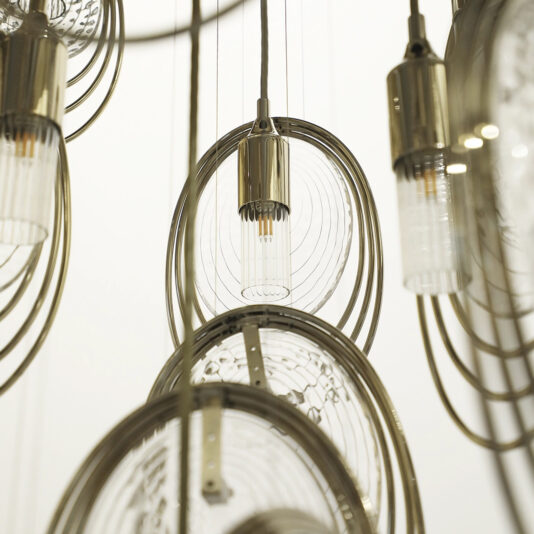 Close-up of the Modern Round Chandelier Inspired By The Sea (Copy), showcasing cylindrical bulbs, concentric metallic rings, and clear circular elements against a neutral backdrop.