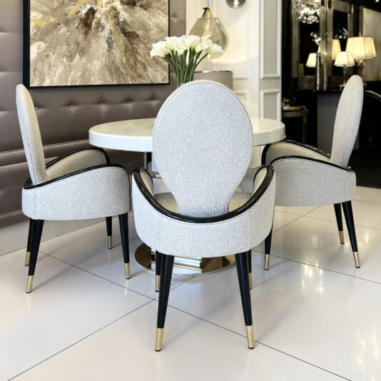 A modern dining area showcases the Mother Of Pearl Exclusive Round Dining Set with three upholstered chairs, a round white table, a vase of white flowers, an abstract painting, and soft lighting for an elegant look.