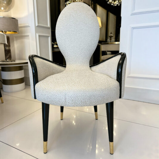 A stylish chair with a high, oval backrest and textured white upholstery stands next to the Mother Of Pearl Exclusive Round Dining Set in a modern, contemporary interior.