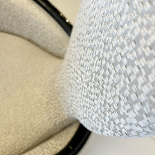 Close-up of the Mother Of Pearl Exclusive Round Dining Set chair, highlighting its textured light upholstery and elegant curved design, with a focus on the fabric pattern and seat edge.