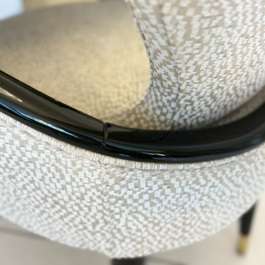 A close-up shows the Mother Of Pearl Exclusive Round Dining Set chair, with a curved black glossy armrest and light geometric-patterned upholstery. The image highlights the textured backrest and part of the seat.