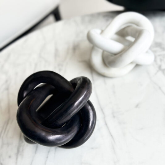 Set Of Luxury Marble Knot Ornaments Two intertwined ceramic knots rest on marble, the black one in front and the white blurred behind—an elegant scene perfect for displaying beside a Set of 3 Burr Walnut Effect Photo Frames (Copy).