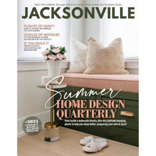 A magazine cover titled “Jacksonville” featuring a cozy home scene with a cushioned bench, decorative pillows, a plant, and slippers on the floor. Headlines highlight summer home design and local stories.