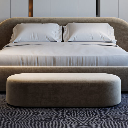 A modern bedroom showcases a large bed with white pillows and sheets, a beige upholstered headboard, and the Contemporary Curved Oval Bench at the foot of the bed, all arranged on a patterned dark rug.