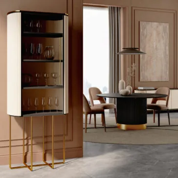 A modern dining room features the Contemporary Lacquered Cabinet (Copy) displaying glassware, a round dining table with sculptural decor, upholstered chairs, large wall art, and floor-to-ceiling curtains.