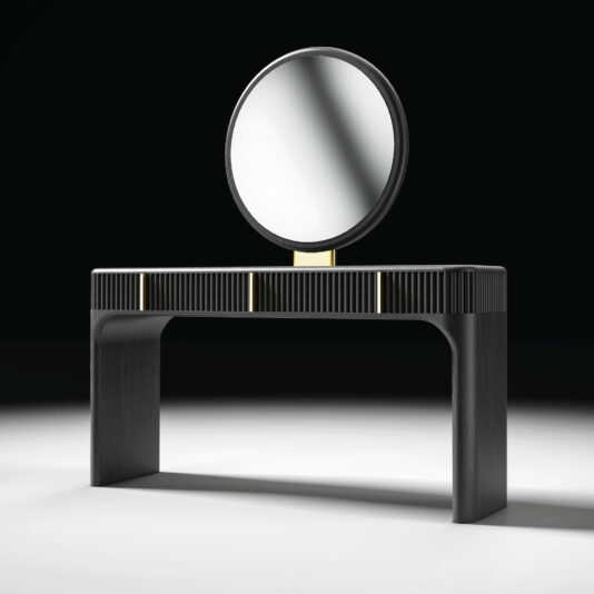The Contemporary Veneered Dressing Table features a large round mirror, gold accents, and ribbed texture, standing on a white surface with a dark background.