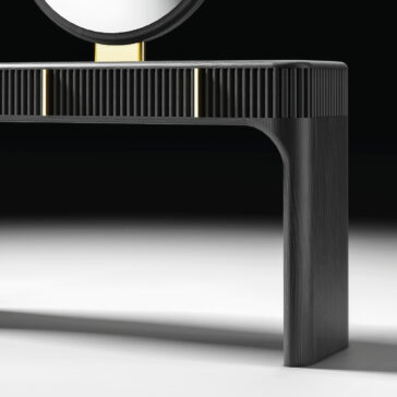 The Contemporary Lacquered Dressing Table features black lacquer, gold accents, rounded edges, a ribbed texture, and a circular mirror. It is shown against a dark background on a white surface.