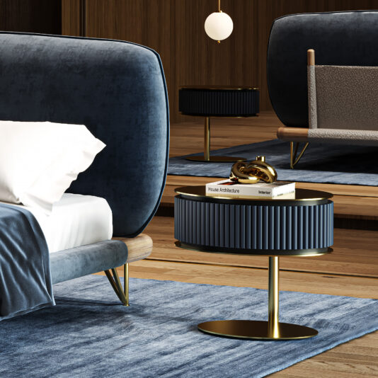 A modern bedroom showcases a blue upholstered bed with a white pillow, a Contemporary Oval Lacquered Bedside table with gold accents, stacked books, a gold decorative item, and a blue rug on wooden flooring; another similar table appears in the background.