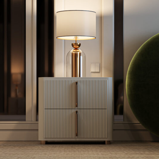 A Contemporary Ribbed Lacquered Bedside Cabinet holds a modern table lamp with a glass base and white shade in a softly lit, stylish room with neutral tones and a touch of green from a nearby chair.