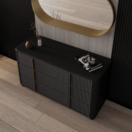 Contemporary Ribbed Lacquered Chest of Drawers A modern black Contemporary Ribbed Lacquered Chest of Drawers stands against a light wood wall, topped with a vase of twigs and magazines, whilst a large oval gold-framed mirror hangs above.