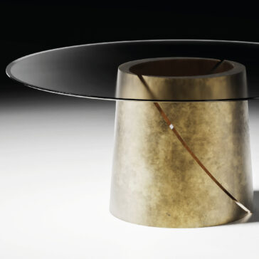 The Contemporary Ebony Veneered Dining Table (Copy) features a modern round design with a transparent glass top and wide cylindrical gold base, accented by a diagonal cut for a sculptural, minimalist look that stands out in neutral spaces.