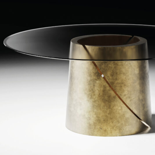 The Contemporary Ebony Veneered Dining Table (Copy) features a modern round design with a transparent glass top and wide cylindrical gold base, accented by a diagonal cut for a sculptural, minimalist look that stands out in neutral spaces.