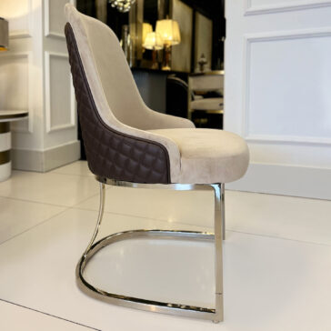 Contemporary Two-Tone Leather Dining Chair The Contemporary Two-Tone Leather Dining Chair features a modern beige seat, quilted dark brown backrest, and shiny metal cantilever base, shown on white tiles in an elegant room with decorative wall panels and lamps.