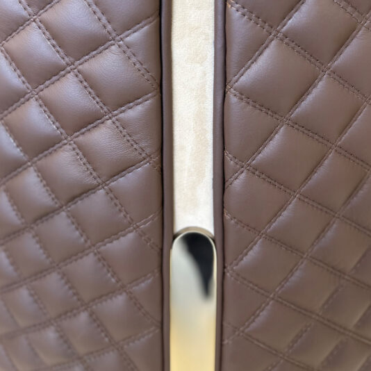 Close-up of the Contemporary Two-Tone Leather Dining Chair, showcasing brown quilted upholstery and a shiny metallic handle with a beige vertical accent in the center.