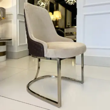 Contemporary Two-Tone Leather Dining Chair The Contemporary Two-Tone Leather Dining Chair features a beige cushioned seat and backrest, brown quilted sides, and a curved chrome base, shown on a white tiled floor in a bright, stylish interior.