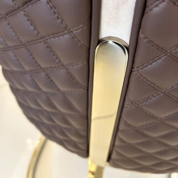 Contemporary Two-Tone Leather Dining Chair Close-up of the quilted brown leather surface from the Contemporary Two-Tone Leather Dining Chair, showing gold metal trim, detailed stitching, and a shiny metallic vertical accent.