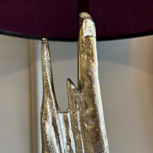 A shiny silver abstract sculpture with pointed shapes sits under the Large Abstract Table Lamp With Velvet Shade, against a blurred cream wall and a dark purple circular object above.