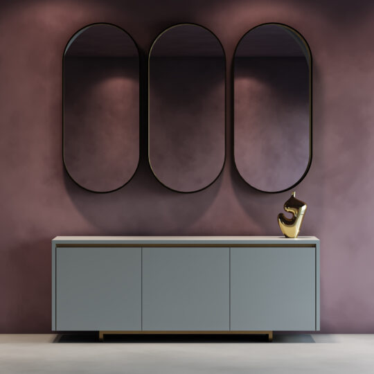 A Contemporary Lacquered Curved Sideboard (Copy) with a matte gray finish stands against a purple-toned wall, topped with a gold abstract sculpture on the right and three tall oval mirrors hanging above.