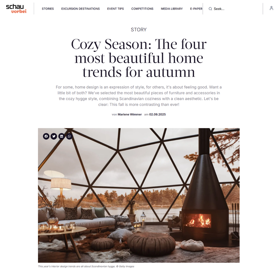 Cozy season article showing a modern living room with large windows, cosy furniture, a round coffee table, and a black suspended fireplace. Neutral tones and Scandinavian decor create a warm, inviting autumn atmosphere.
