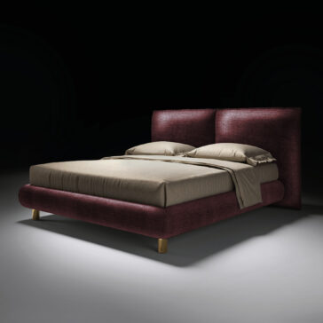 Contemporary Italian Bed The Contemporary Italian Bed features a dark burgundy upholstered frame and headboard, beige bedding with two pillows, and wooden legs, all showcased against a plain black background with dramatic lighting.