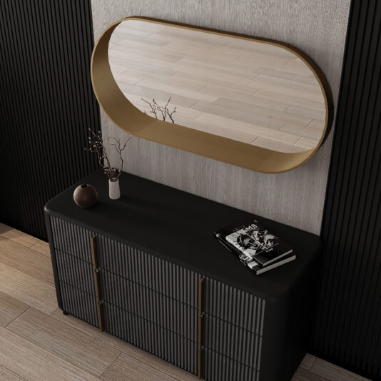 A black console table holds a brown vase with twigs and a magazine. Next to it, a geometric chaise longue sits beneath the Contemporary Pill Wall Mirror, which reflects the light wooden floor and textured walls.