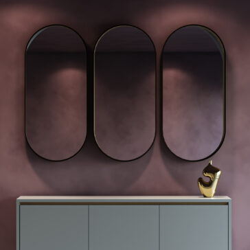 Three oval mirrors hang on a mauve wall above a light gray cabinet, enhanced by a shiny gold abstract sculpture and the Contemporary Geometric Chaise Longue (Copy), creating a modern, elegant look.