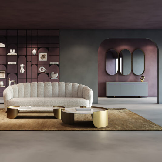 Contemporary Pill Wall Mirror A modern living room with a geometric chaise longue, a curved beige sofa, two round gold-accented coffee tables, and a brown rug. Wall shelves showcase decor, above a sideboard placed beneath three Contemporary Pill Wall Mirrors.