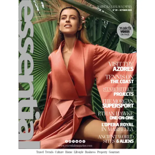 A woman in a coral pink dress sits among large green tropical leaves on the cover of Essential Magazine, October 2025. Feature articles and topics are listed beside her on the right.