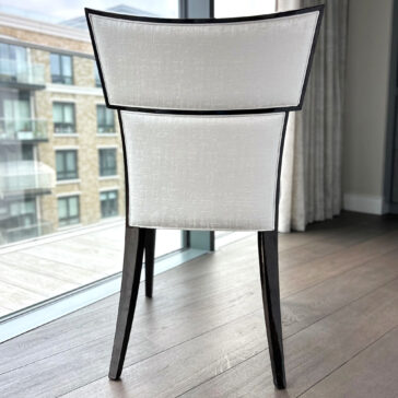 Classic Deco Style Dining Chair The Classic Deco Style Dining Chair features light upholstery and dark legs, set on wooden flooring by large windows with views of a block of flats.