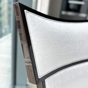 Classic Deco Style Dining Chair The Classic Deco Style Dining Chair features light textured upholstery and a dark wooden frame, shown near a large window with an urban view in the background.