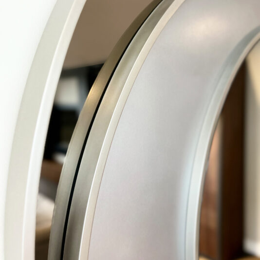 Contemporary Italian Designer Offset Circles Mirror Close-up of the edge of the Contemporary Italian Designer Offset Circles Mirror (Copy), featuring a metallic frame and reflecting part of a room with blurred furniture in the background.