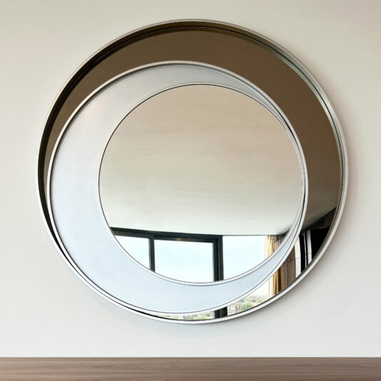 Contemporary Italian Designer Offset Circles Mirror The Contemporary Italian Designer Offset Circles Mirror (Copy), featuring overlapping circular frames, is mounted on a wall and reflects windows and a neutrally decorated, naturally lit room.