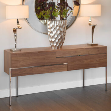 Contemporary Walnut Veneer Sideboard The Contemporary Walnut Veneer Sideboard with metal legs is styled with a large metallic vase of green and burgundy plants, two tall white-shaded lamps, and a round mirror hanging above.
