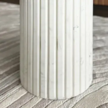 A close-up of a cylindrical white marble column with vertical grooves stands on a textured, striped surface beside the Exclusive Ammonite Tuscany Quartz Coffee Table.