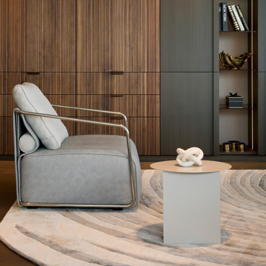 High Quality Hand Woven Swirl Rug A modern living room with a light grey armchair, round side table topped with a white knot sculpture, wooden cupboards, shelves of books and decor—all anchored by the High Quality Hand Woven Swirl Rug and stylish patterned accents.