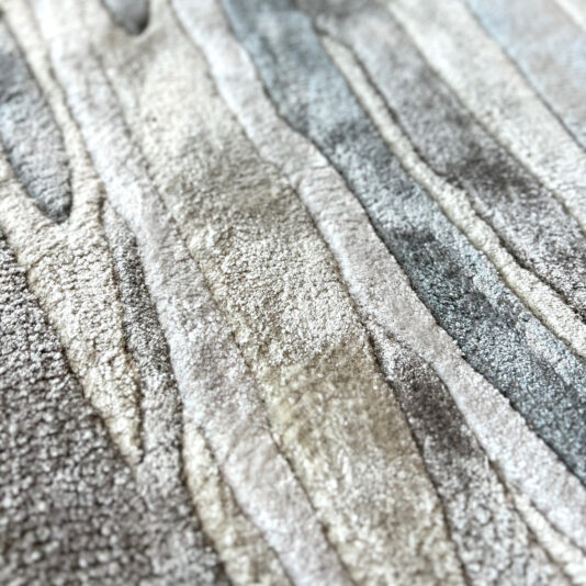 High Quality Hand Woven Swirl Rug Close-up of the High Quality Hand Woven Swirl Rug, showcasing textured, abstract wavy patterns in grey, beige, and light blue tones that evoke natural stone or wood grain.