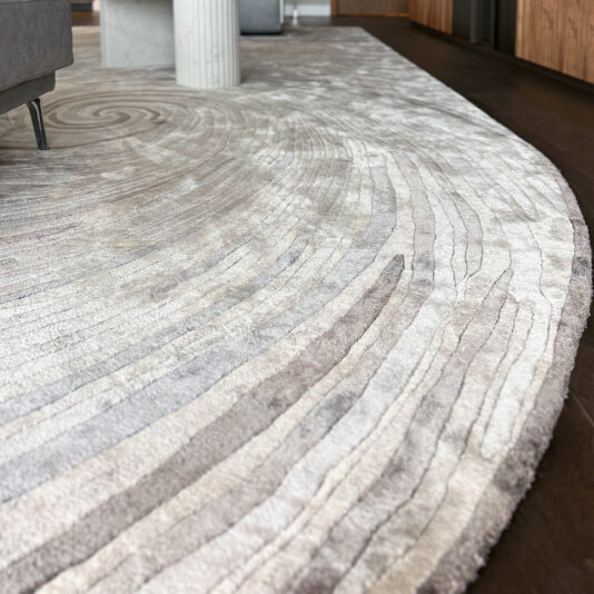 High Quality Hand Woven Swirl Rug A close-up of the High Quality Hand Woven Swirl Rug shows its plush, light-coloured fibres and textured patterns laid on a dark wooden floor in a stylish modern interior.
